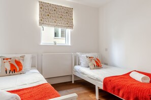 A small, clean room with two single beds, a window with a view, and a radiator. - Lakeside Villa w/ Pool & Tennis in Cotswolds (Gloucestershire)