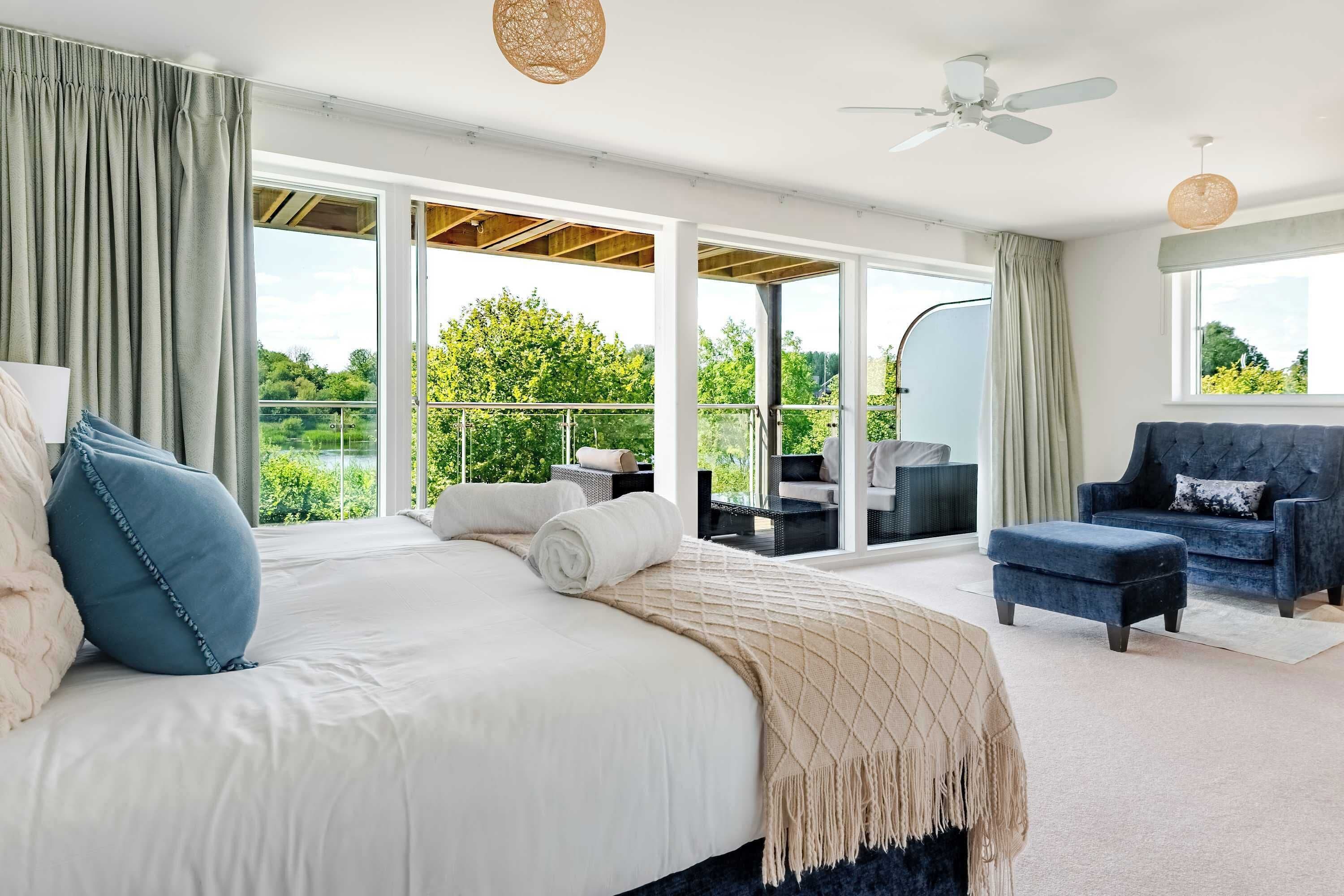 Ein Schlafzimmer mit einem großen Bett, einem Balkon, einer Sitzecke und Blick auf Grünflächen.