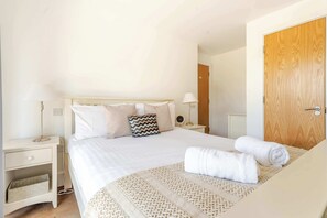 A hotel room with a bed, bedside tables, a lamp, a wooden door, and a wall socket. - Lakeside Villa w/ Pool & Tennis in Cotswolds (Gloucestershire)