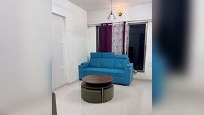 A living room with a blue sofa, a round coffee table, and a window with curtains. - lavender residense MIDC andheri east (Mumbai)