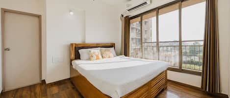 A bedroom with a wooden bed, a ceiling fan, an air conditioning unit, and a large window with curtains.