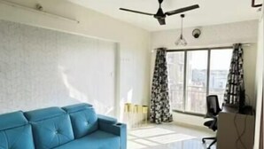 A modern living room with a blue sofa, a round coffee table, a ceiling fan, and a view through a window with curtains. - lavender residense MIDC andheri east (Mumbai)