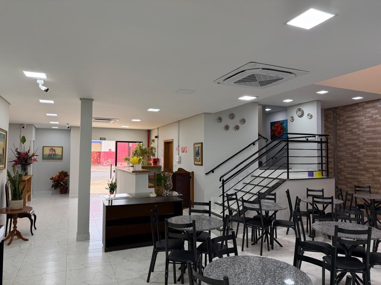Um saguão de hotel com balcão de recepção, várias áreas de estar e uma escadaria.