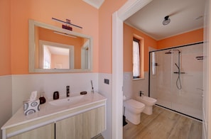 Un bany amb un mirall gran, un lavabo, un vàter i una zona de dutxa.