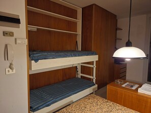A bunk bed with a wooden wardrobe, a bedside table with a lamp, and a wall-mounted thermostat. - Punta Ala: Studio Apartment with Ocean View - Climate - Parking Space - Beaches (Punta Ala)