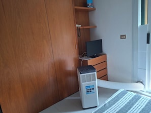 Une pièce avec une armoire en bois, un bureau doté d’un écran d’ordinateur et un radiateur mobile.