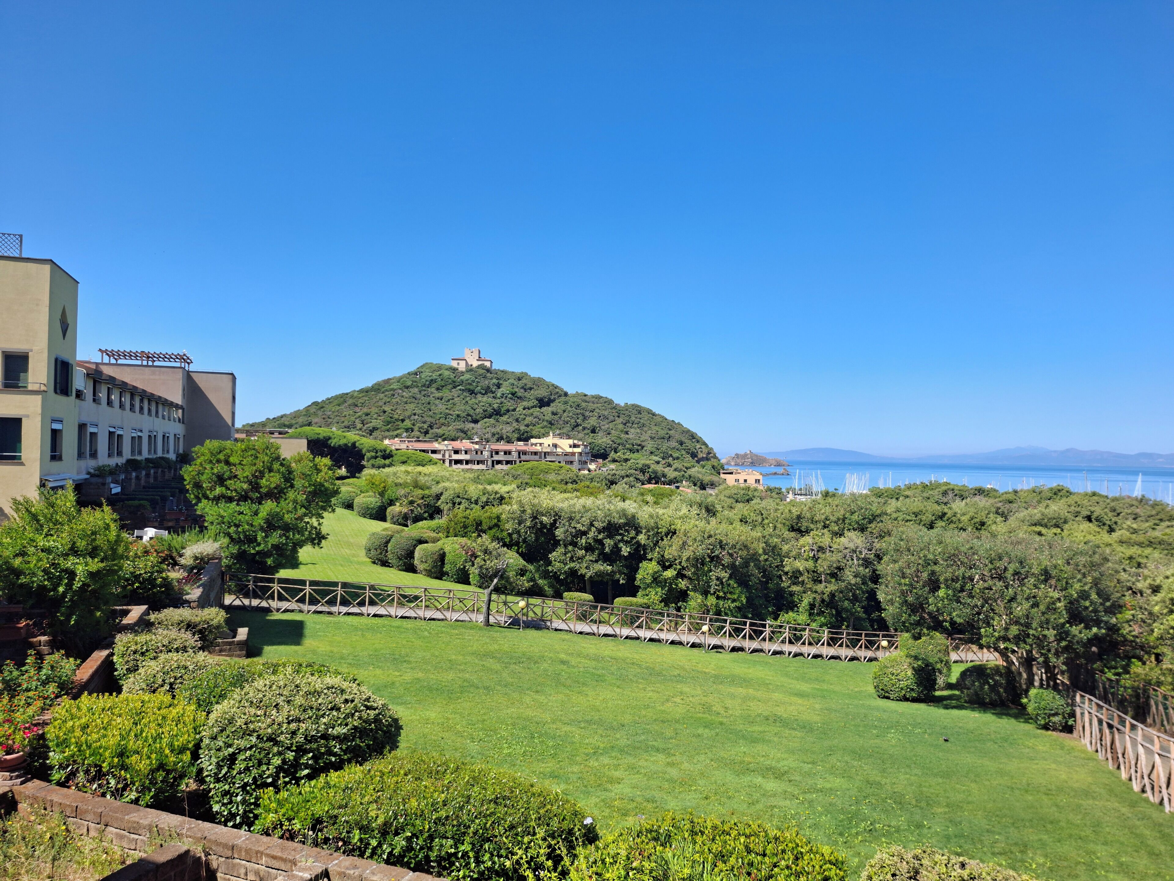 Une colline surmontée d’un château, entourée de verdure et sous un ciel bleu clair.