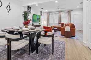 A modern living room with a dining area, featuring a sofa set, a coffee table, and a dining table with chairs. - The Retreat at Drew | 3 En Suites Beds + Workspace (Houston)