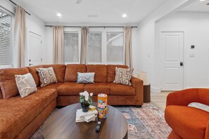 A modern living room with a sectional sofa, a coffee table, and a small orange chair. - The Retreat at Drew | 3 En Suites Beds + Workspace (Houston)