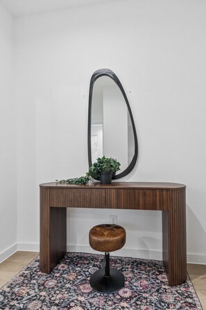 A wooden console table with a mirror, a potted plant, and a stool. - The Retreat at Drew | 3 En Suites Beds + Workspace (Houston)