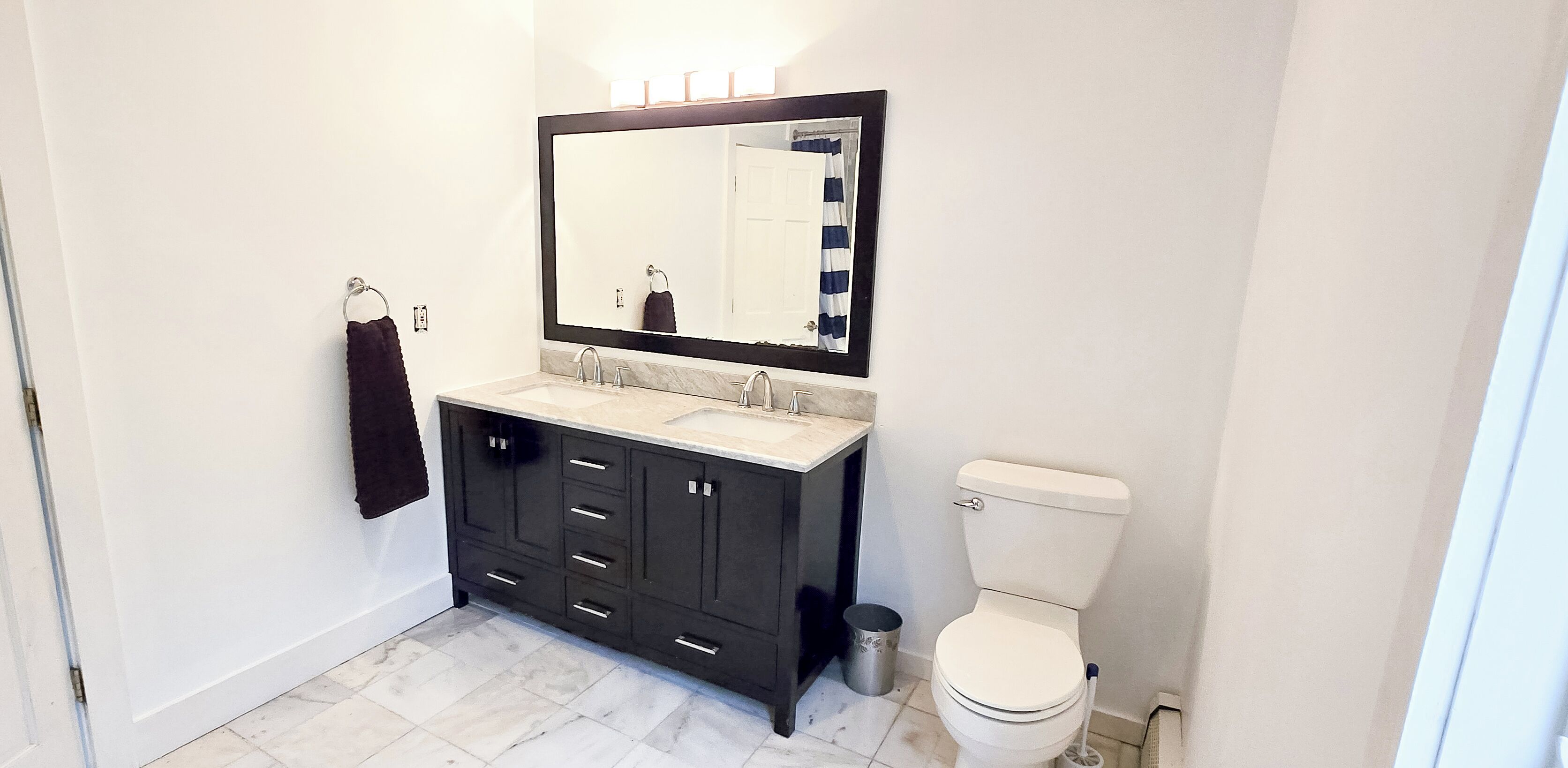 A bathroom with a double sink vanity, a toilet, and a large mirror.