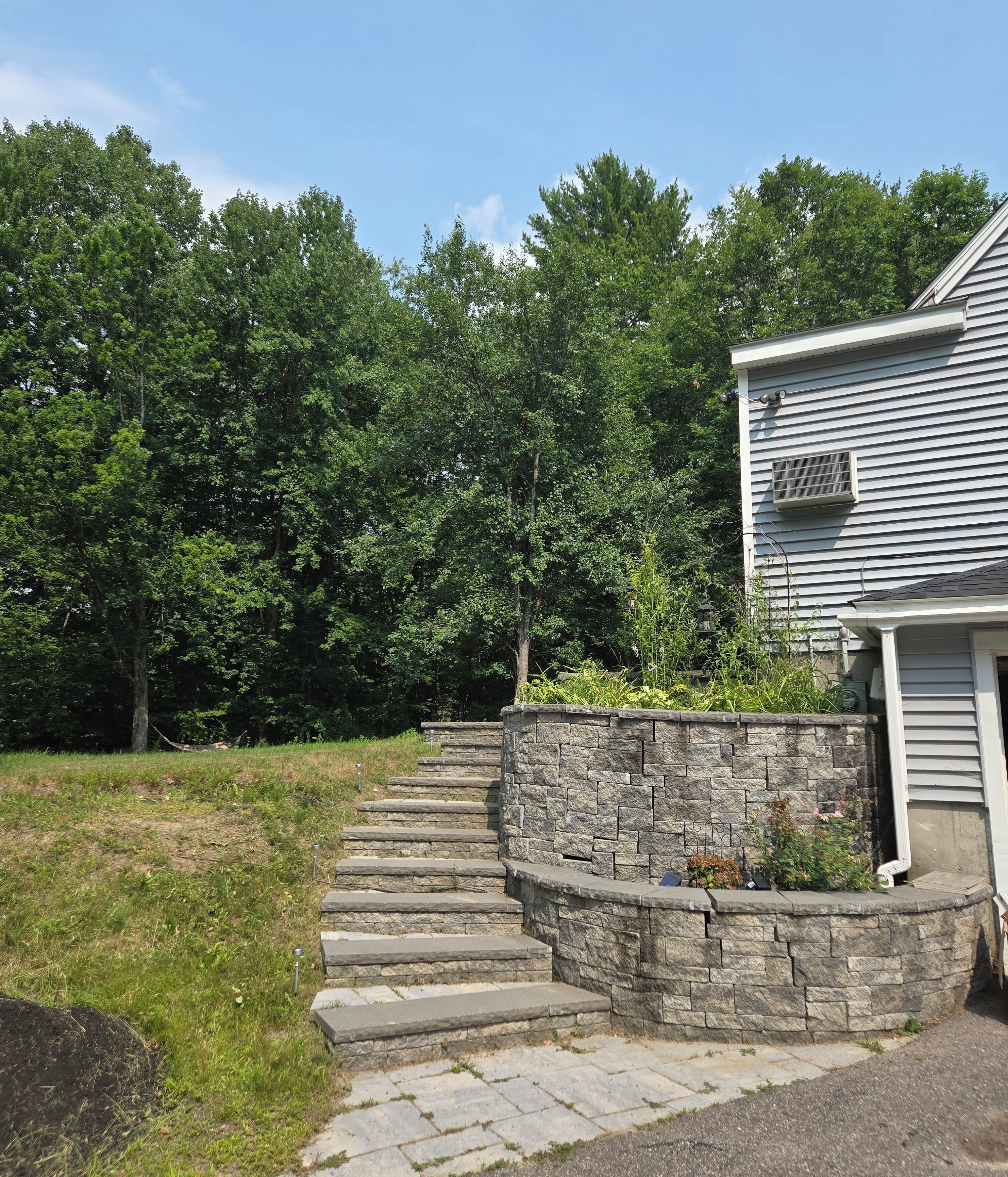 A stone staircase leading to a house with a garage, surrounded by a grassy area and dense trees.