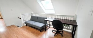 A room with a wooden floor, a grey sofa, a black office chair, a small table, and a white railing. - Spacious home a stones throw from Newfound Lake (Bristol)