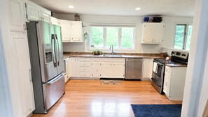 A kitchen with white cabinets, a stainless steel refrigerator, a dishwasher, and a stove. - Spacious home a stones throw from Newfound Lake (Bristol)