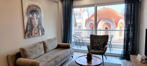 A living room with a sofa, a chair, a coffee table, and a large window with a view of traditional architecture. - Premium apartment in Acropolis (Athens)