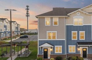 A multi-story residential building with a parking lot, a streetlight, and a cellular tower in the background. - Flames Fan House | *3 MIN to LU* | Sleeps 10! (Lynchburg)