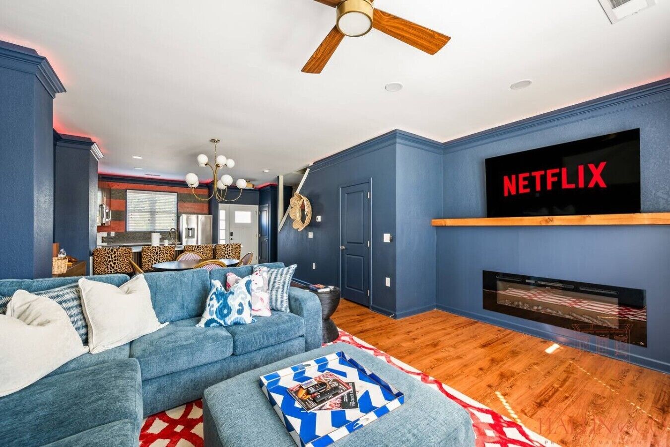 A modern living room with a blue sofa, a coffee table with magazines, a fireplace, and a mounted TV screen displaying 'NETFLIX'.