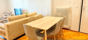 A modern living room with a beige sofa, a wooden dining table, and matching chairs. - Sunny home in Acropolis (Athens)