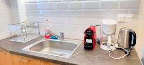 A kitchen with a stainless steel sink, a red coffee maker, a white coffee pot, and a dish rack with plastic containers. - Sunny home in Acropolis (Athens)