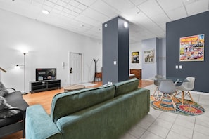 A modern living room with a green sofa, a TV displaying a movie, and a poster on the wall. - Boutique-Style Studio in the heart of the Old Port (Montréal)