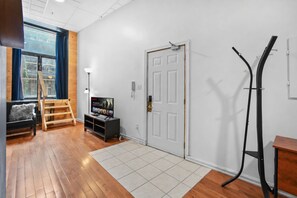 A room with a wooden floor, a white door, a TV on a stand, a ladder, and a window with curtains. - Boutique-Style Studio in the heart of the Old Port (Montréal)