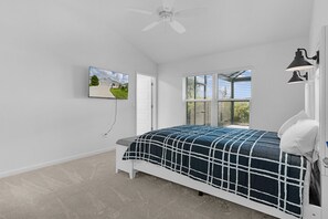 Ein Schlafzimmer mit einem Bett, einem an der Wand montierten Fernseher, einem Deckenventilator und einem Fenster mit Jalousien.