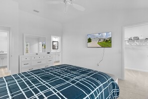Un dormitorio con cama, cómoda, espejo, ventilador de techo y televisor montado en la pared.