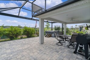 An outdoor patio with a covered seating area, a grill, and a TV screen. - Dog-Friendly 3BR Designer Home with Spa & 4-Seat Golf Cart (The Villages)
