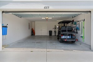 A garage with a golf cart parked inside, a door with the number 685, and a bicycle leaning against the wall. - Dog-Friendly 3BR Designer Home with Spa & 4-Seat Golf Cart (The Villages)