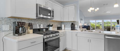 Una cocina moderna con armarios blancos, estufa de acero inoxidable, microondas integrado y cafetera.