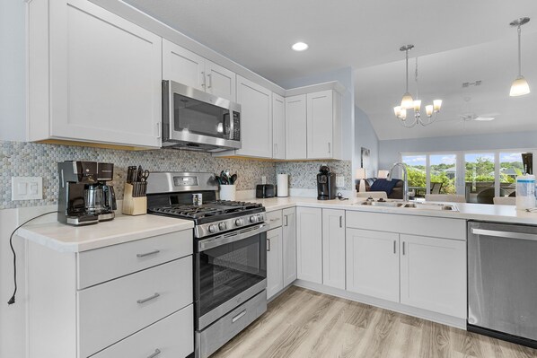 Una cocina moderna con armarios blancos, estufa de acero inoxidable, microondas integrado y cafetera.