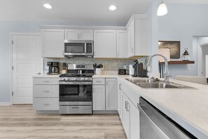 A modern kitchen with white cabinetry, stainless steel appliances, and a wooden floor. - Dog-Friendly 3BR Designer Home with Spa & 4-Seat Golf Cart (The Villages)
