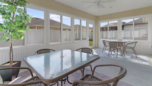 A covered patio with a glass-top table and wicker chairs, surrounded by large windows. - Dog-Friendly Citrus Grove Home with Golf Cart, Fenced Yard & Lanai (The Villages)