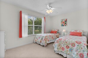 Ein Schlafzimmer mit zwei Betten, einem Deckenventilator, einem Fenster mit Jalousien und einer Wandlampe.