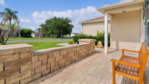 Una propiedad residencial con un patio empedrado, un banco de madera, un muro de contención de piedra y un garaje.