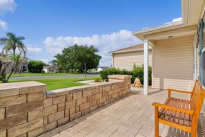 Ein Wohnhaus mit gepflasterter Terrasse, einer Holzbank, einer Steinmauer und einer Garage.