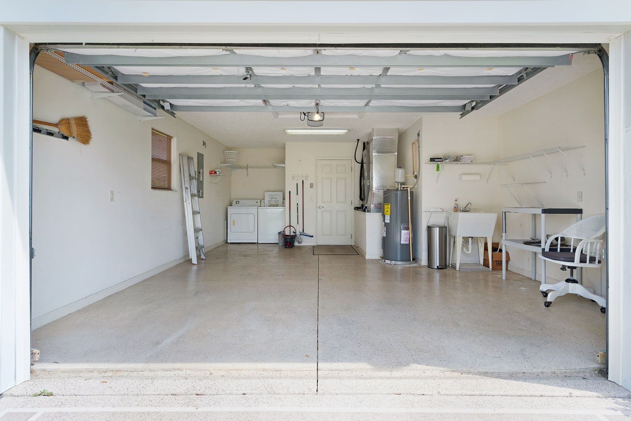 A garage with a washing machine, a heater, and a chair.