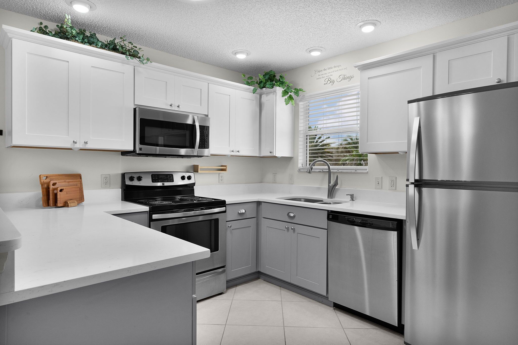 A modern kitchen with stainless steel appliances, white cabinetry, and a window with blinds.