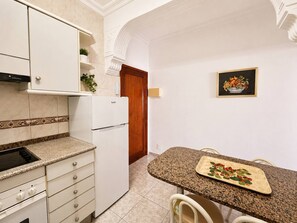 A kitchen with white cabinets, a granite countertop, a built-in stove, and a refrigerator. - Las Canteras | 1 Min to the Beach | Ocean View | 2 Guests (Las Palmas de Gran Canaria)