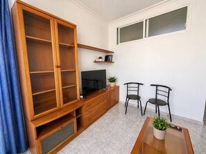 A living room with a wooden cabinet, a television, two chairs, a coffee table, and a window. - Las Canteras | 1 Min to the Beach | Ocean View | 2 Guests (Las Palmas de Gran Canaria)
