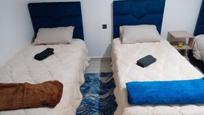 Two single beds with blue headboards, a small bedside table with a lamp, and a blue patterned rug. - Hostel Dar Khelifa (TÉTOUAN)