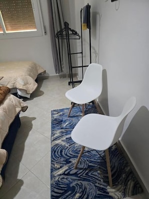 A room with a bed, two white chairs, a patterned rug, and a coat rack. - Hostel Dar Khelifa (TÉTOUAN)