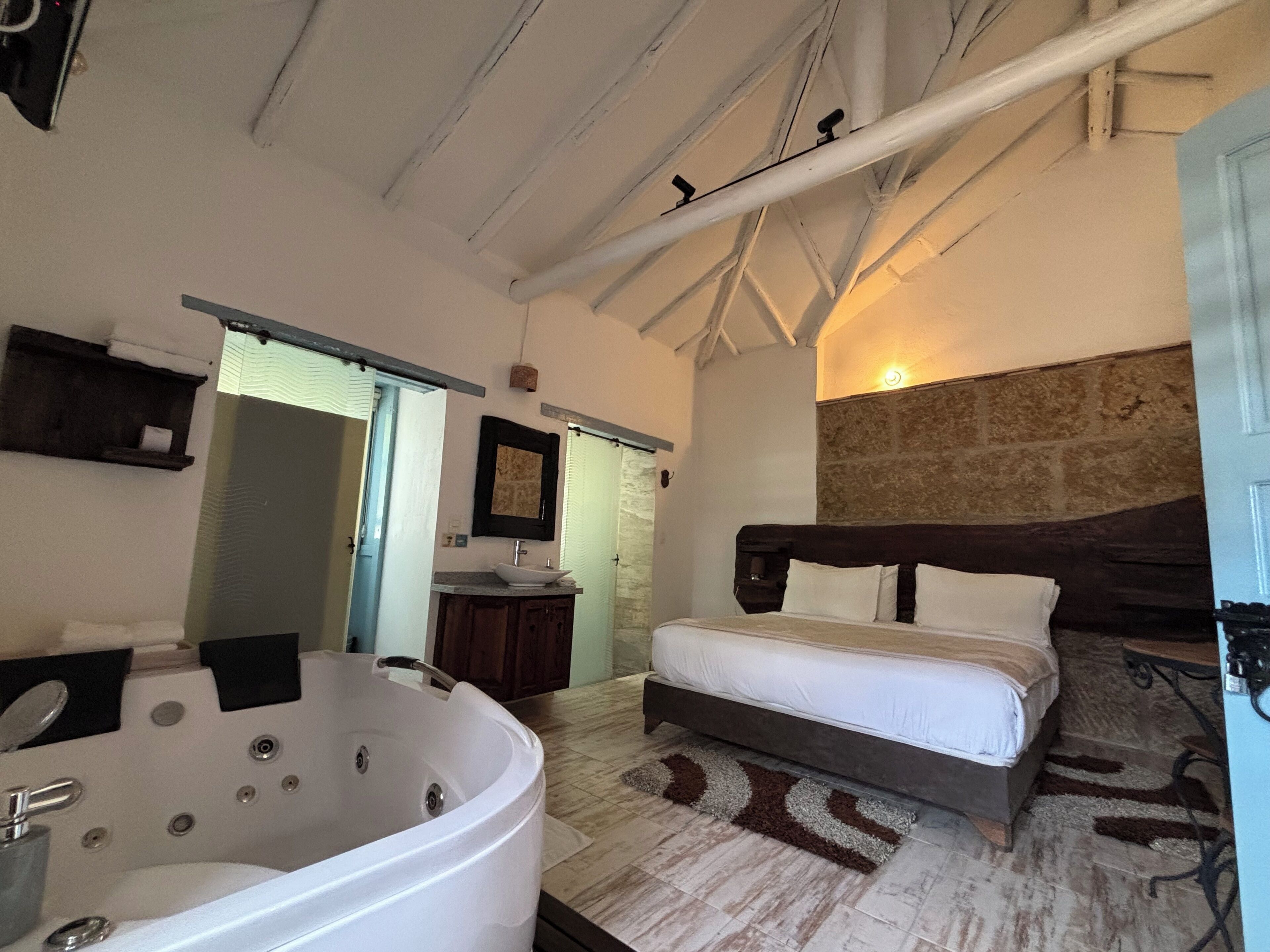 Une chambre avec une grande baignoire, un lit double et un mur décoratif en pierre.