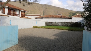 A courtyard with a gravel path, white brick walls, and a mountain in the background. - Hotel Boutique Santa Helena (Villa de Leyva)