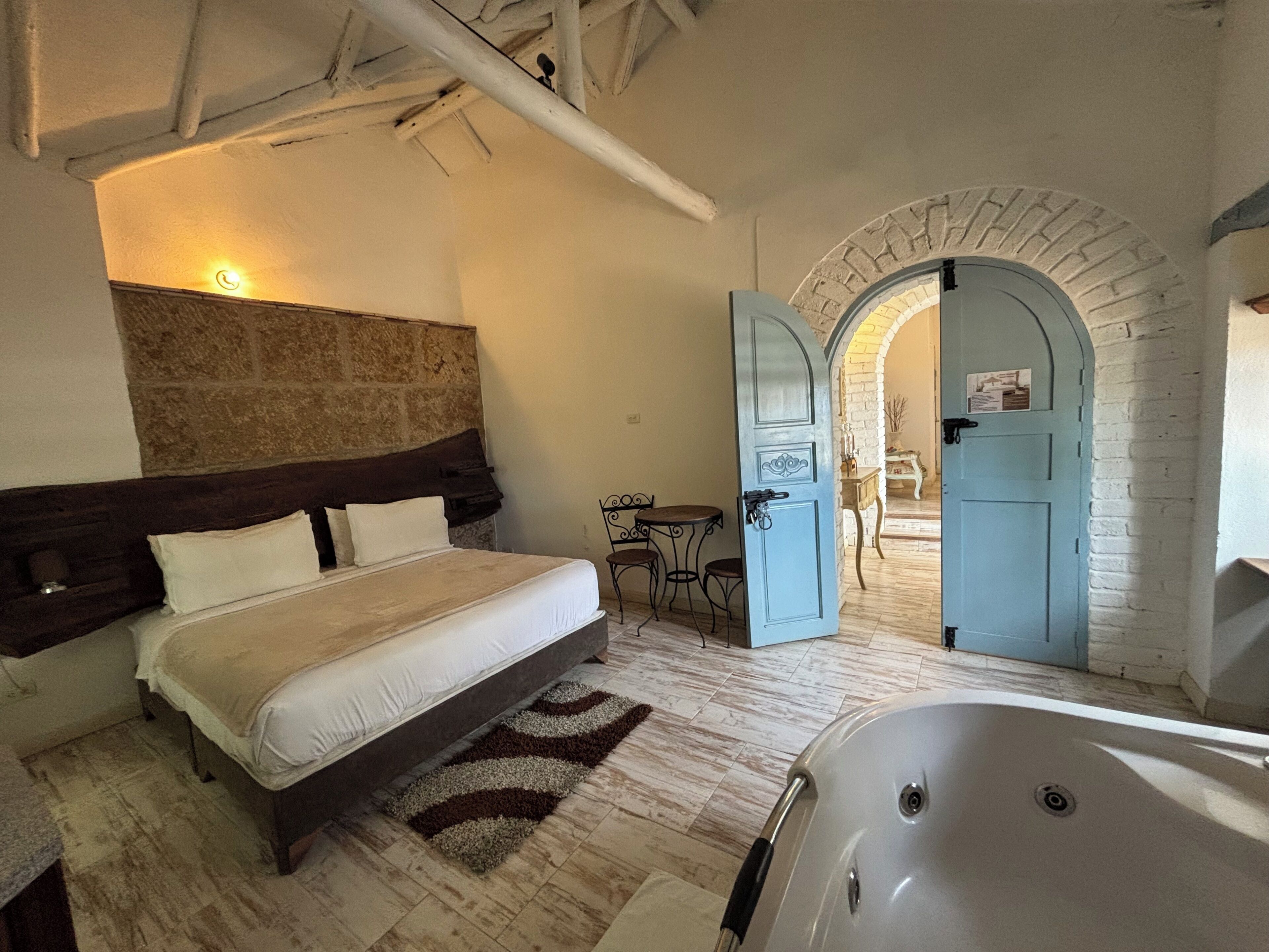 A bedroom with a large bed, a sitting area with a table and chairs, and a bathroom with a bathtub.