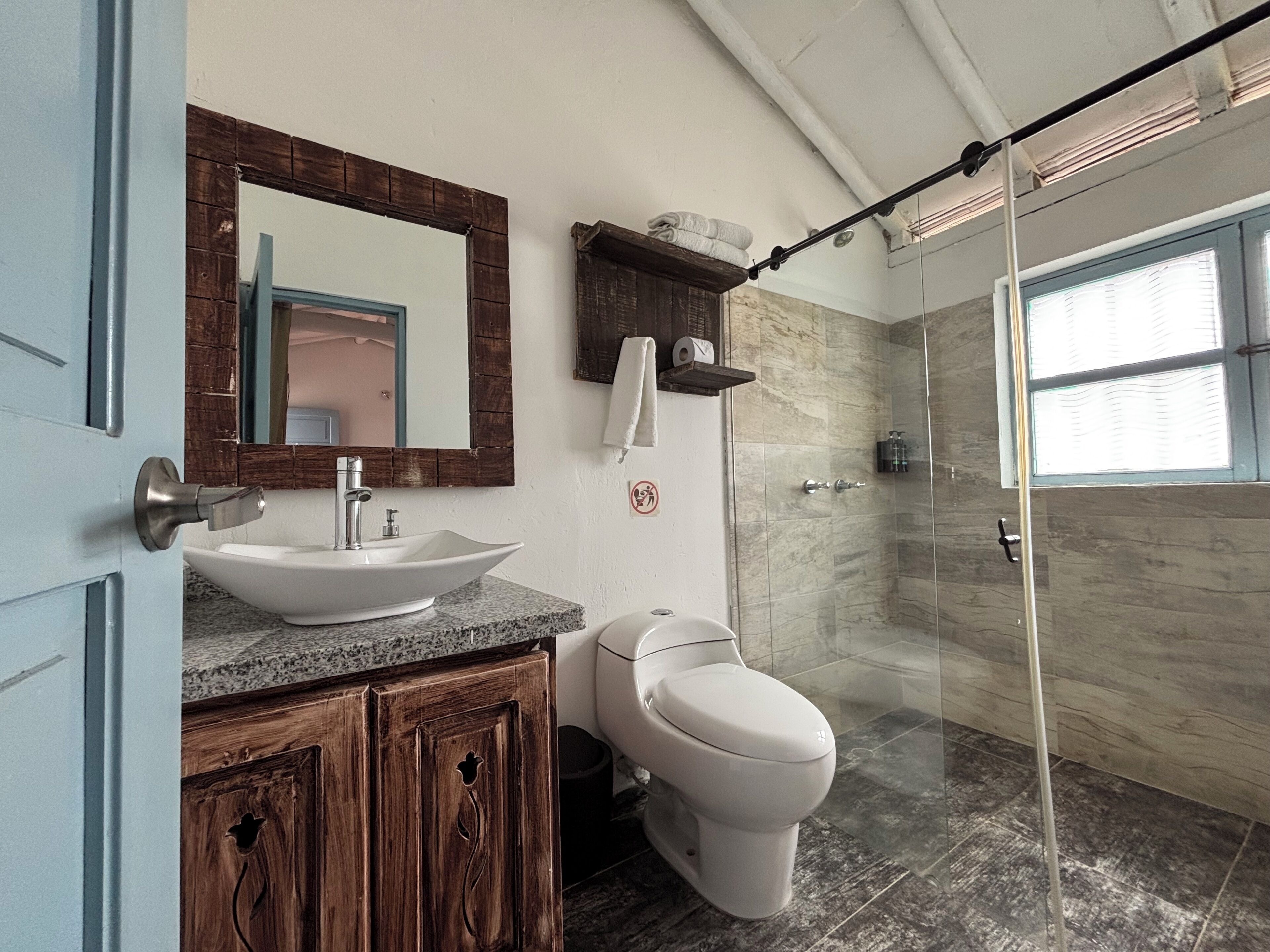 Ein Badezimmer mit einem Aufsatzwaschbecken, Holzschränken, einer Toilette, einer Dusche mit Glastüren und einem Spiegel mit Holzrahmen.