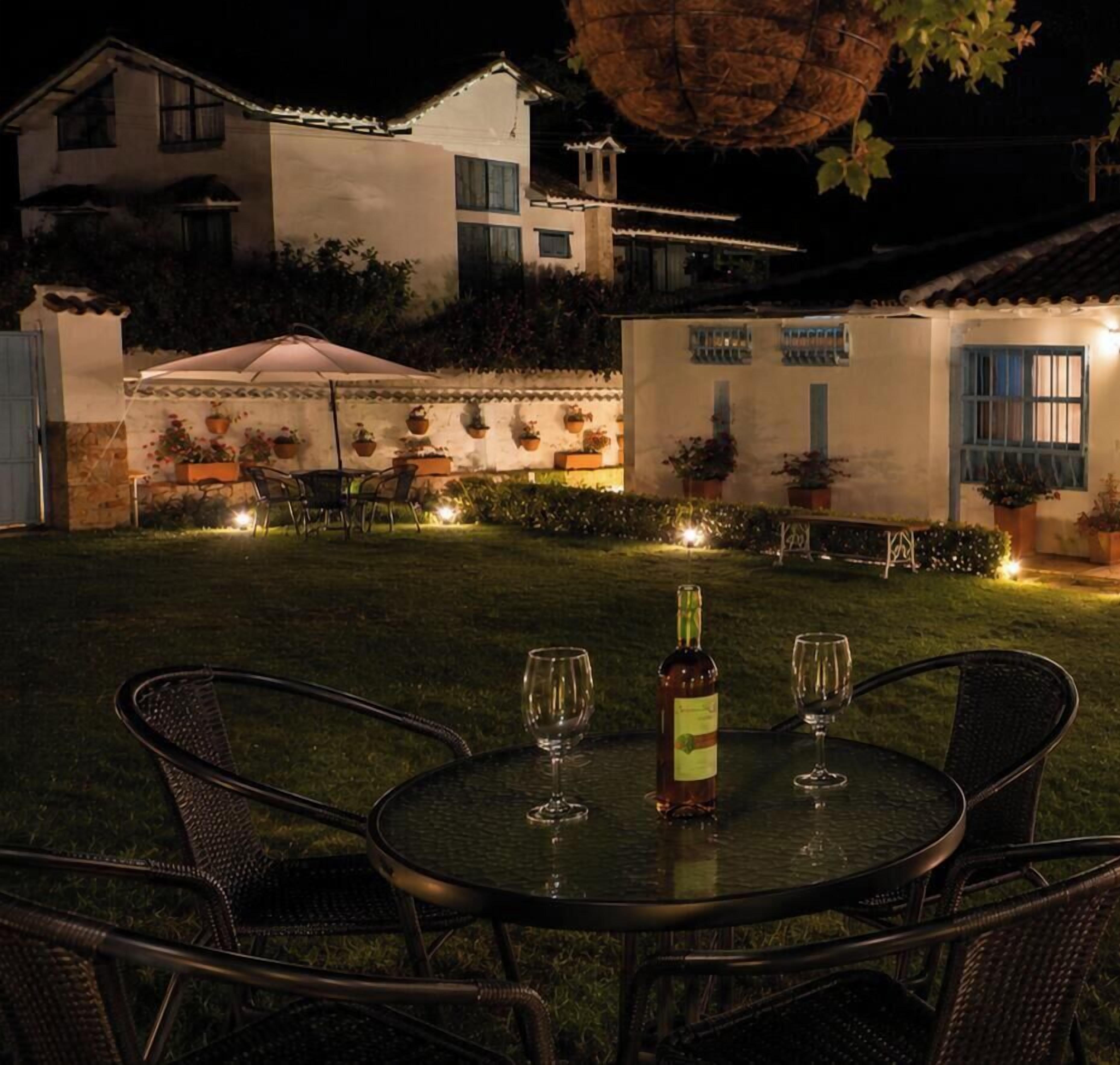 An outdoor dining area with a table and chairs, a bottle of wine, and potted plants.