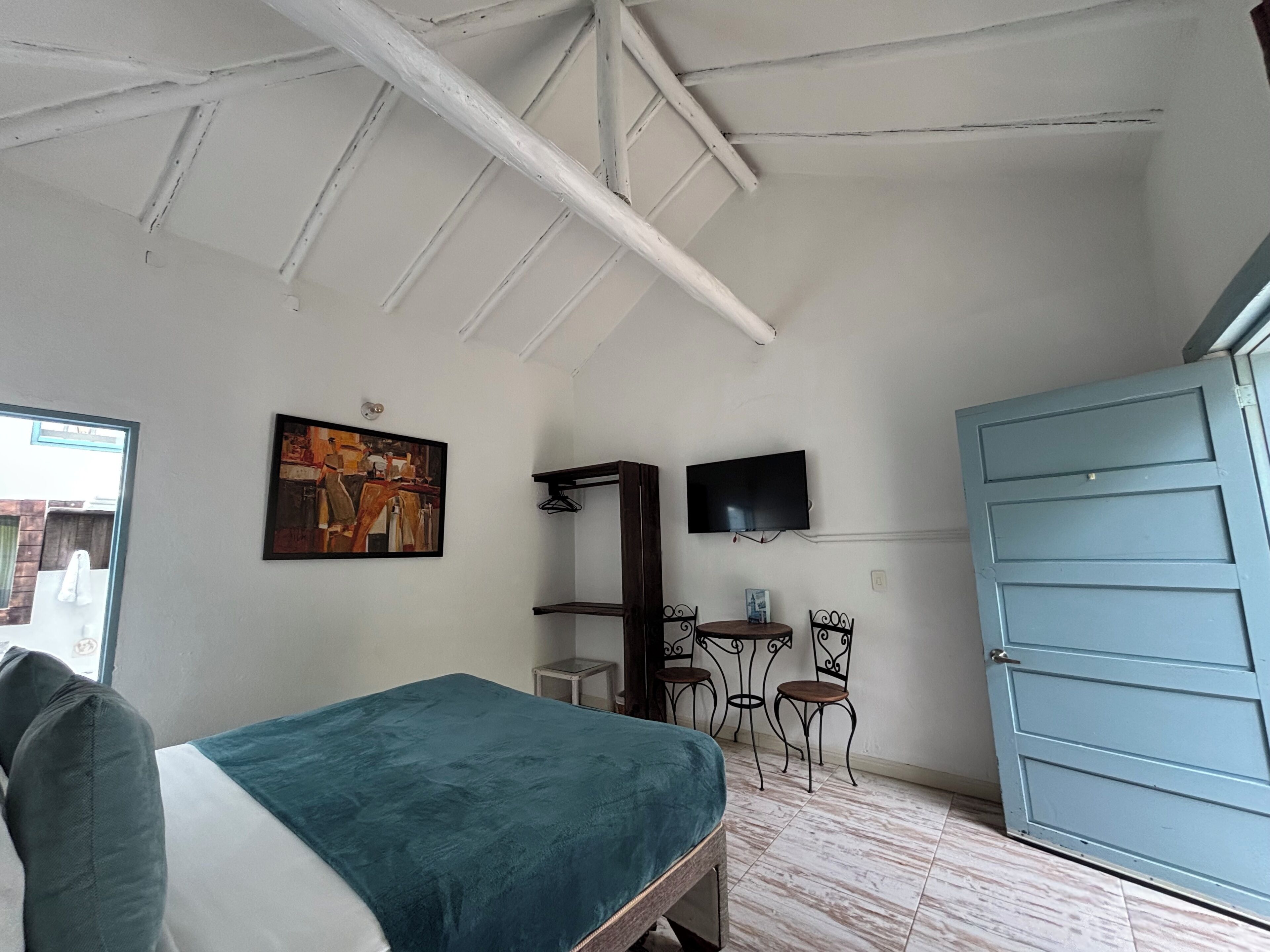 A bedroom with a bed, a painting, a TV, a desk, and a wardrobe.