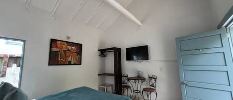 A bedroom with a bed, a painting, a TV, a desk, and a wardrobe.