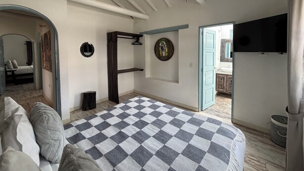 A bedroom with a checkered bedspread, a wooden wardrobe, a mirror, and a television on the wall. - Hotel Boutique Santa Helena (Villa de Leyva)